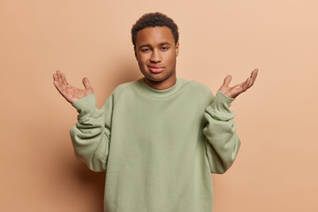 Horizontal shot of dark skinned handsome adult man spreads palms ponders perplexing decision...