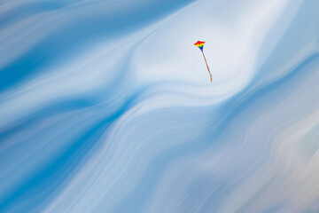 Rainbow kite against a blue cloudy sky, and the sky is streaked after the fashion of photographer...