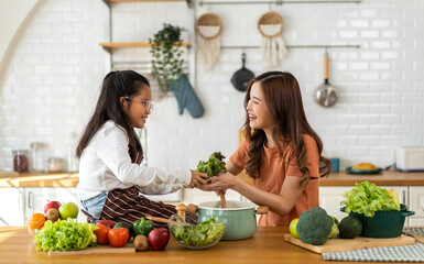 Portrait of happy love asian family mother with little asian girl daughter child help cooking food healthy eat with fresh vegetable testing smell soup in a pot with spoon.helping mommy in kitchen