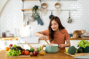 Young woman standing near stove and cooking, housewife, meal, chef, food.Happy woman looking and smelling tasting fresh delicious from soup in a pot with steam at white interior kitchen