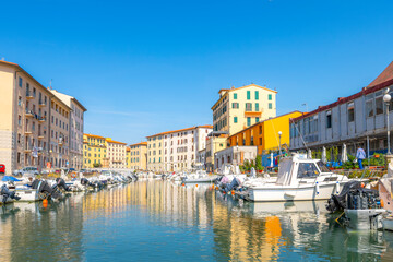 Fototapeta na wymiar Colorful residential buildings reflect off the water in the boat filled canals at the old port of Livorno, Italy, in the Tuscany region.