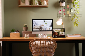 Stylish workplace with computer, laptop and lamp near olive wall at home