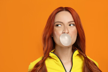 Portrait of beautiful woman blowing bubble gum on orange background. Space for text