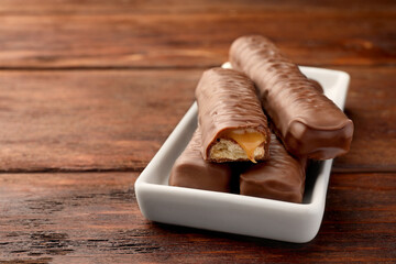 Sweet tasty chocolate bars with caramel on wooden table, closeup. Space for text