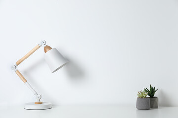 Stylish modern desk lamp and potted succulents on table near white wall indoors