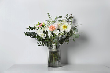 Bouquet of beautiful flowers in vase on table against white wall