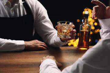 Bartender giving glass of whiskey to customer at bar counter, closeup