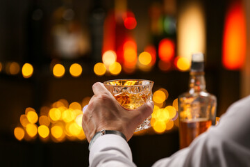 Man with glass of whiskey against blurred lights, closeup