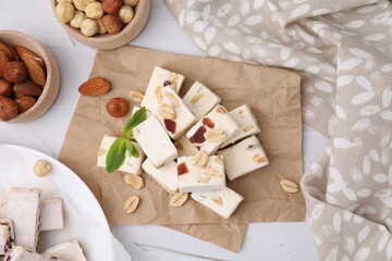 Pieces of delicious nutty nougat, hazelnuts and almonds on white table, flat lay