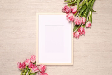 Empty photo frame and beautiful tulip flowers on wooden background, flat lay. Mockup for design