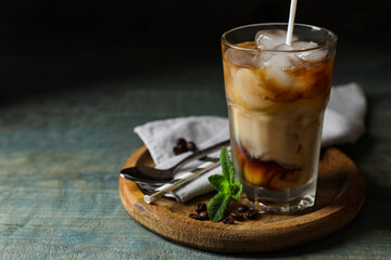 Pouring milk into glass of delicious iced coffee, mint and beans on light blue wooden table, space for text