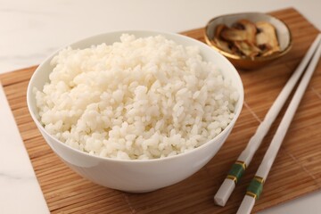 Bowl with delicious rice, mushrooms and chopsticks on white table, closeup