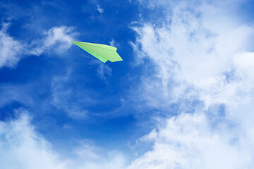 Naklejka na ściany i meble White clouds and paper airplane flying in blue sky on sunny day. Space for text