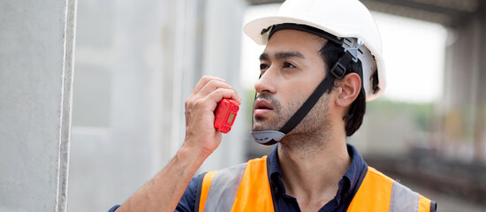 Young man engineer using radio command with worker in construction site, architect or contractor speak to radio for control and planning development structure at precast factory, industrial concept.