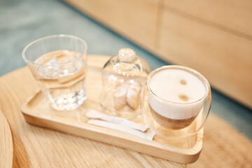 Cup of coffee cappuccino with cantuccini and a glass of water on a wooden tray. Coffee with milk, a cookie and a glass with water on a glass table.