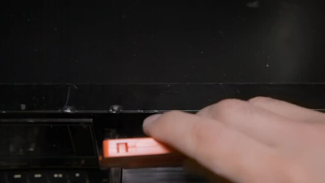 A hand removing a transparent cassette tape and inserting an orange one into a stereo deck player. Top view.