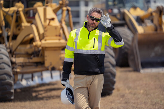 Machinery Builder At Buildings Background. Excavator Loader Tractor And Buider Worker. Portrait Of Worker Man Small Business Owner. Construction Worker With Hardhat Helmet On Construction Site.