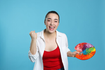 Woman with paint palette on light blue background. Young artist