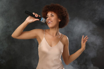 Curly young woman with microphone singing in smoke on black background