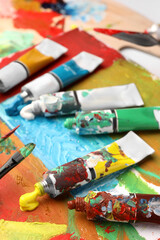 Tubes of colorful oil paints and brushes on canvas with abstract painting, closeup