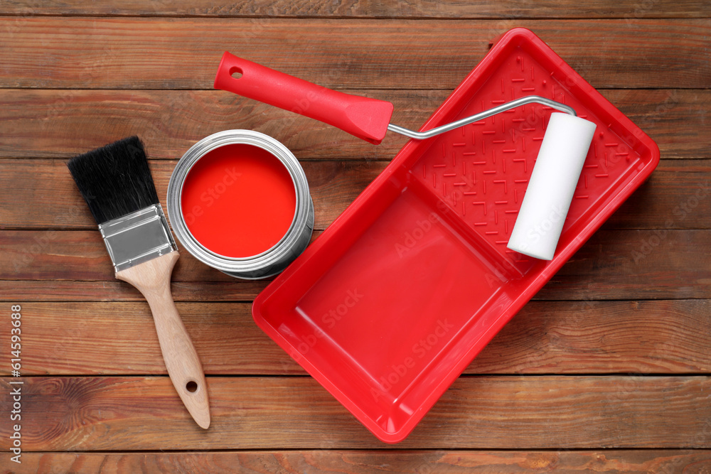 Sticker Can of red paint, brush, roller and tray on wooden table, flat lay