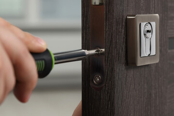Handyman with screwdriver repairing door lock indoors, closeup
