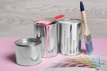 Cans of paints, brushes and color palette on pink wooden table
