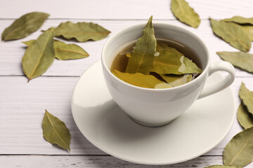 Cup of freshly brewed tea with bay leaves on white wooden table, closeup