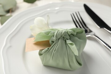 Furoshiki technique. Gift packed in green fabric with flower and blank card on plate, closeup