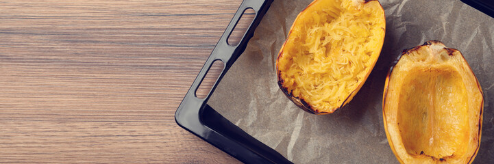Baking sheet with halves of cooked spaghetti squash on wooden table, top view. Banner design with space for text