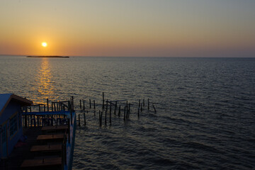 Sunrise overlooking Fishing dock in Cedar Key Florida. On a sunny day with calm waters. Wood pier poles in water with dim lights.