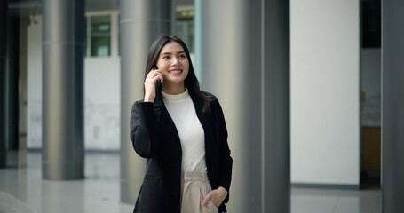 Young Asian businesswoman in suit talking on  smartphone while walking