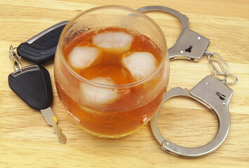 Glass of whisky with handcuffs and car key on wooden background.