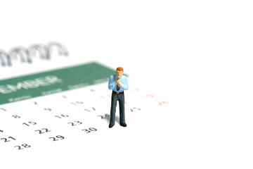 Miniature tiny people toy figure photography. A businessman getting ready, justify the tie standing above calendar. Isolated on white background