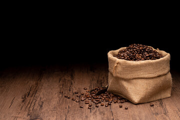 Fototapeta na wymiar The many coffee beans and bag and scoop are placed around on a wooden table in a warm, light atmosphere, on dark background, with copy space.