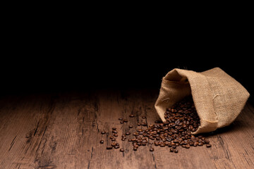 The many coffee beans and bag and scoop are placed around on a wooden table in a warm, light...