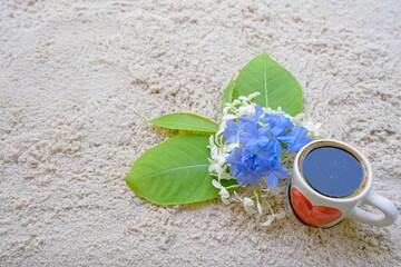 Cup espresso with bouquet flowers on the beach at sea shore.                               