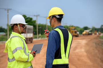 Civil engineers discuss the job with construction foreman while using technology tablet at highway road construction site.