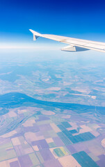 Obraz premium Aerial view from airplane window above green ground. View from the airplane window with beautiful clouds at sunrise
