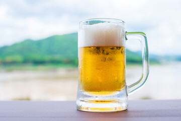 Glass of light beer on a table with nature background.