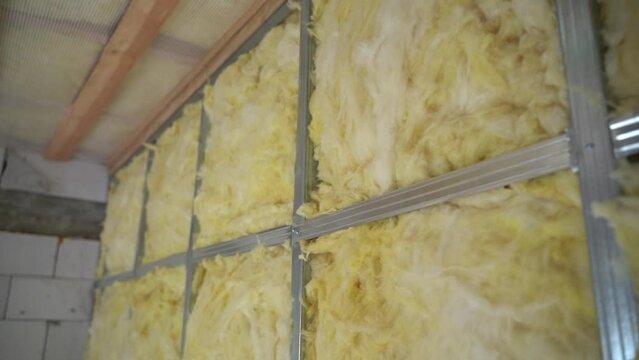 A strong metal frame made of a metal profile for plasterboard finishing is filled with glass wool, close-up. Soundproofing and thermal insulation of the wall between rooms