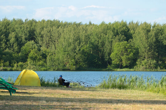 A man is fishing in nature with a tent. Men's rest by the lake. Lots of rods.