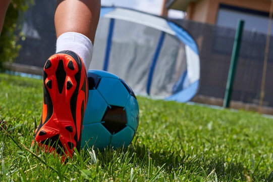 Leg of a girl playing soccer in her backyard with orange boots and blue ball. Orange sole of a soccer boot on the foot of a girl.
