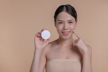 Portrait of a young Asian woman smiling holding mockup product for advertising text place, beige background. Concept of healthcare for skin, beauty care product for advertising.