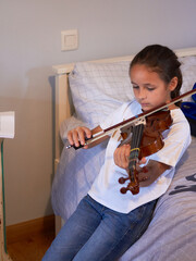 Violin class at home. Little girl practicing violin in her room