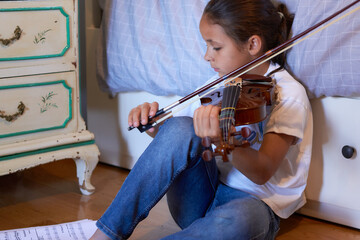 Young girl is playing violin sitting on the floor of her bedroom. Horizontal composition.