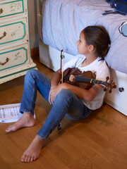 Young girl is sitting on the floor of her bedroom tired from practicing her violin lesson.