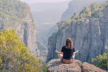 Young girl meditating in lotus yoga pose on top of the cliff overlooking scenic view of Tazi canyon in Turkey