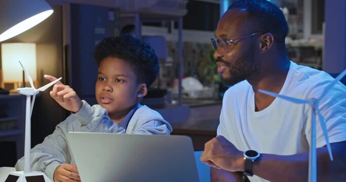 African american businessman and father using computer teaching and explains to his son how wind turbines work. Kids learning about eco-friendly forms of renewable energy. Technology and education.