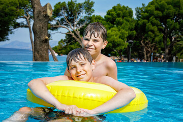 Two kids boys having fun on inflatable rubber rings in outdoor pool. Summer holiday. Summertime kids weekend. Children having fun, brothers on family vacations.